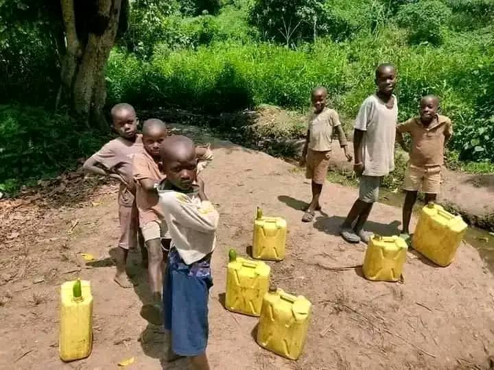 Children standing beside yellow water jerrycans on a dirt path