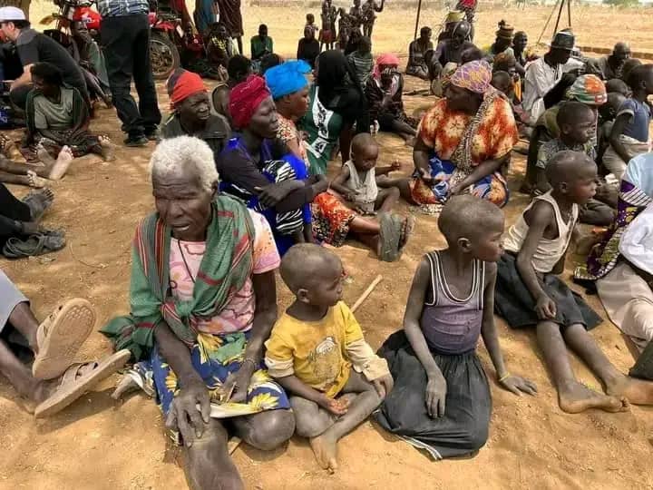 Elderly women and children seated on the ground at a community gathering