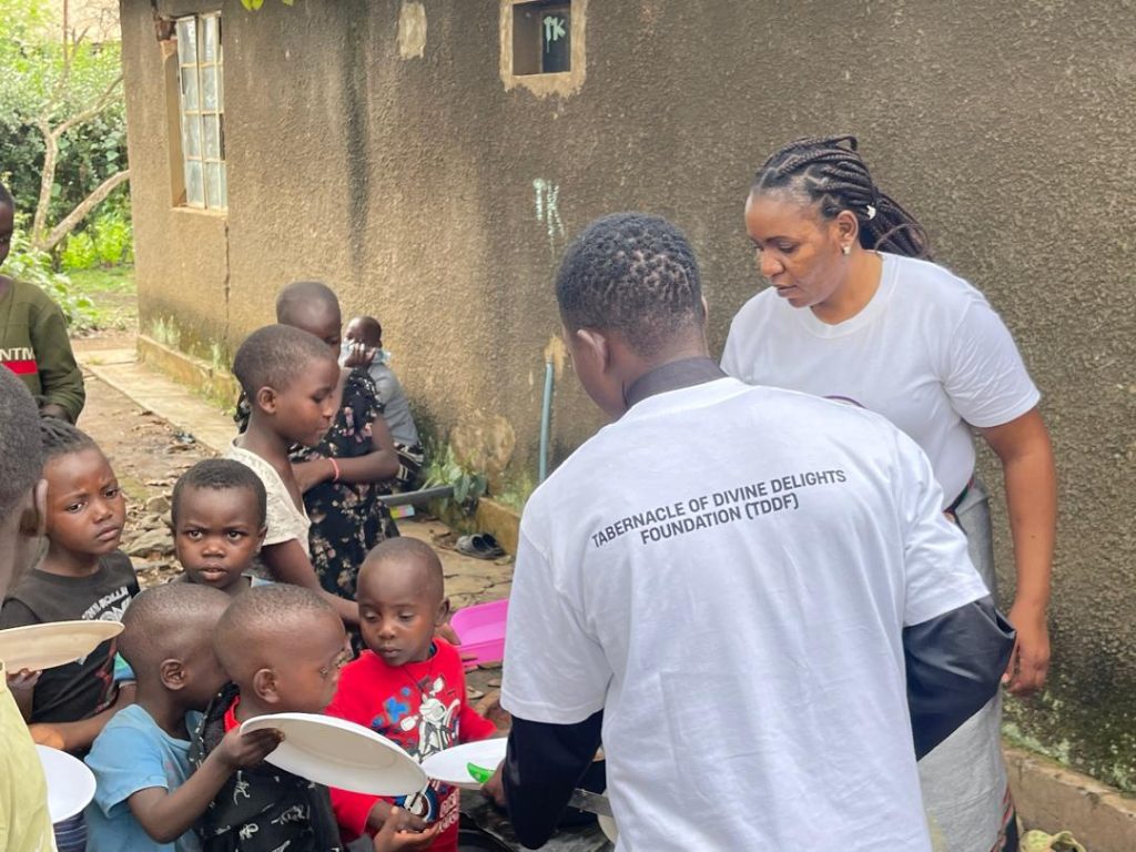 TDD Foundation volunteers serving food to a line of young children outside a house